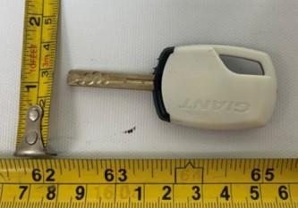 Recalled black-and-white Giant illuminated bicycle-lock key, shown beside measuring tapes in the CPSC notice
